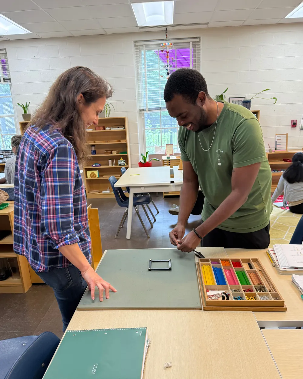 Two adults exploring geometric shapes with colored sticks on a tabletop work mat.