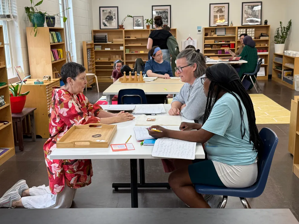 Adults working together with Montessori materials and reference notes around classroom tables.