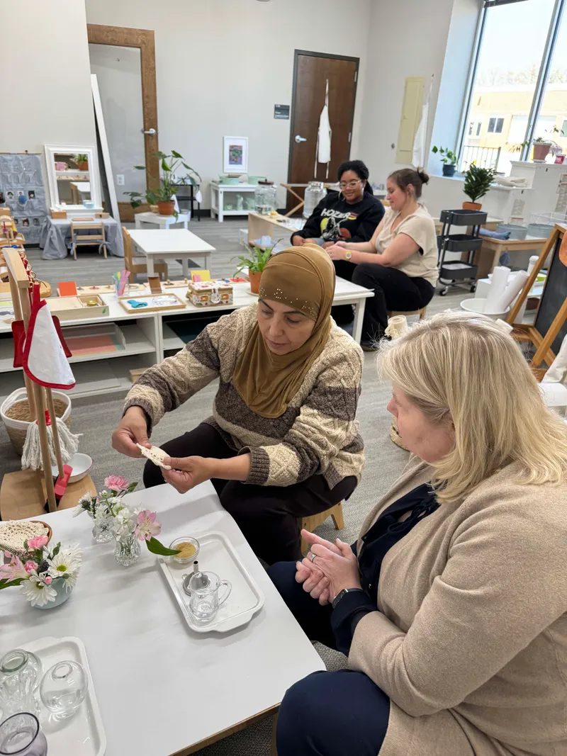 Adults practicing a table activity with small glass pitchers and dishes in an infant and toddler training environment.