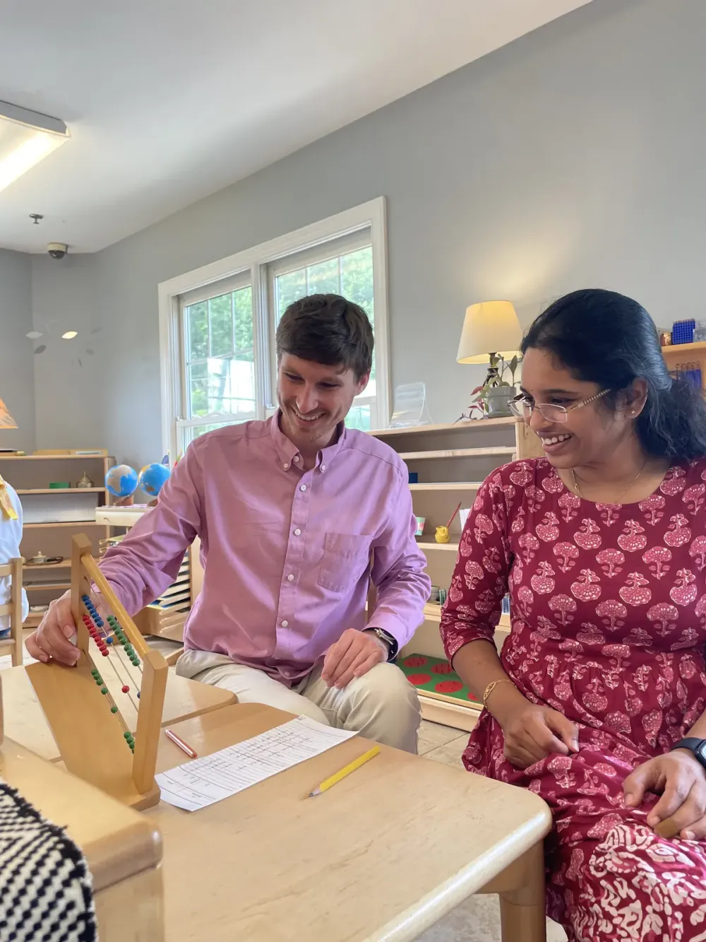 Adults practicing with Montessori materials on a classroom rug.